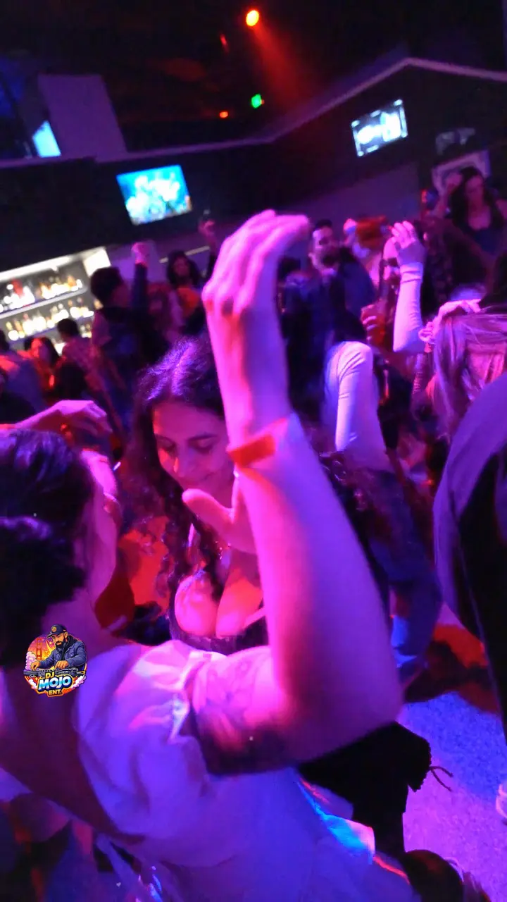 Guests dancing with their hands up under pink and purple club lights in Redding, and DJ Mojo at the turntables