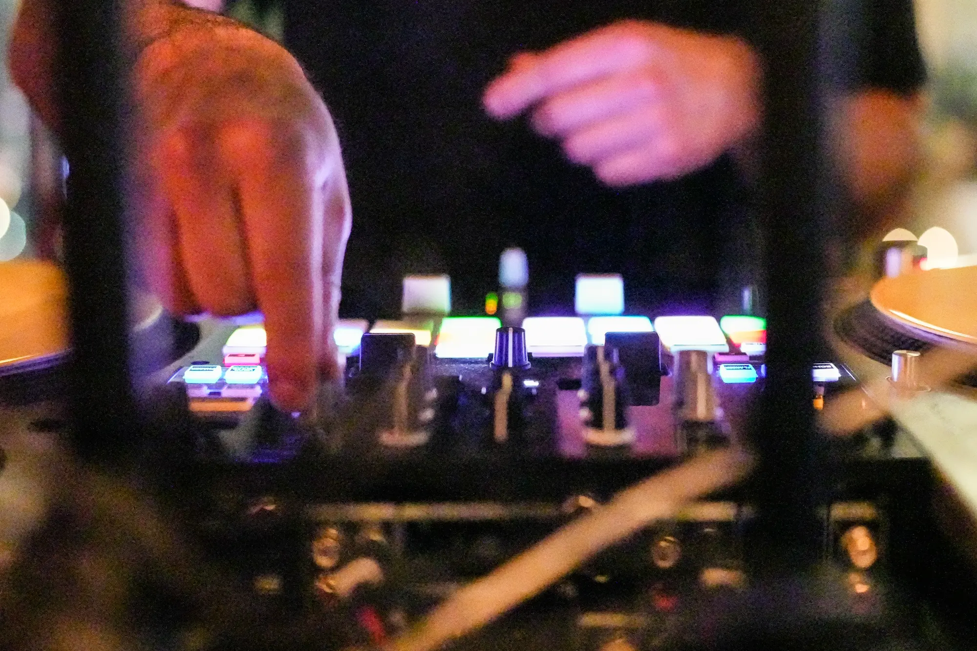 Close view of DJ Mojo's hands on a colorfully lit DJ mixer and turntable.