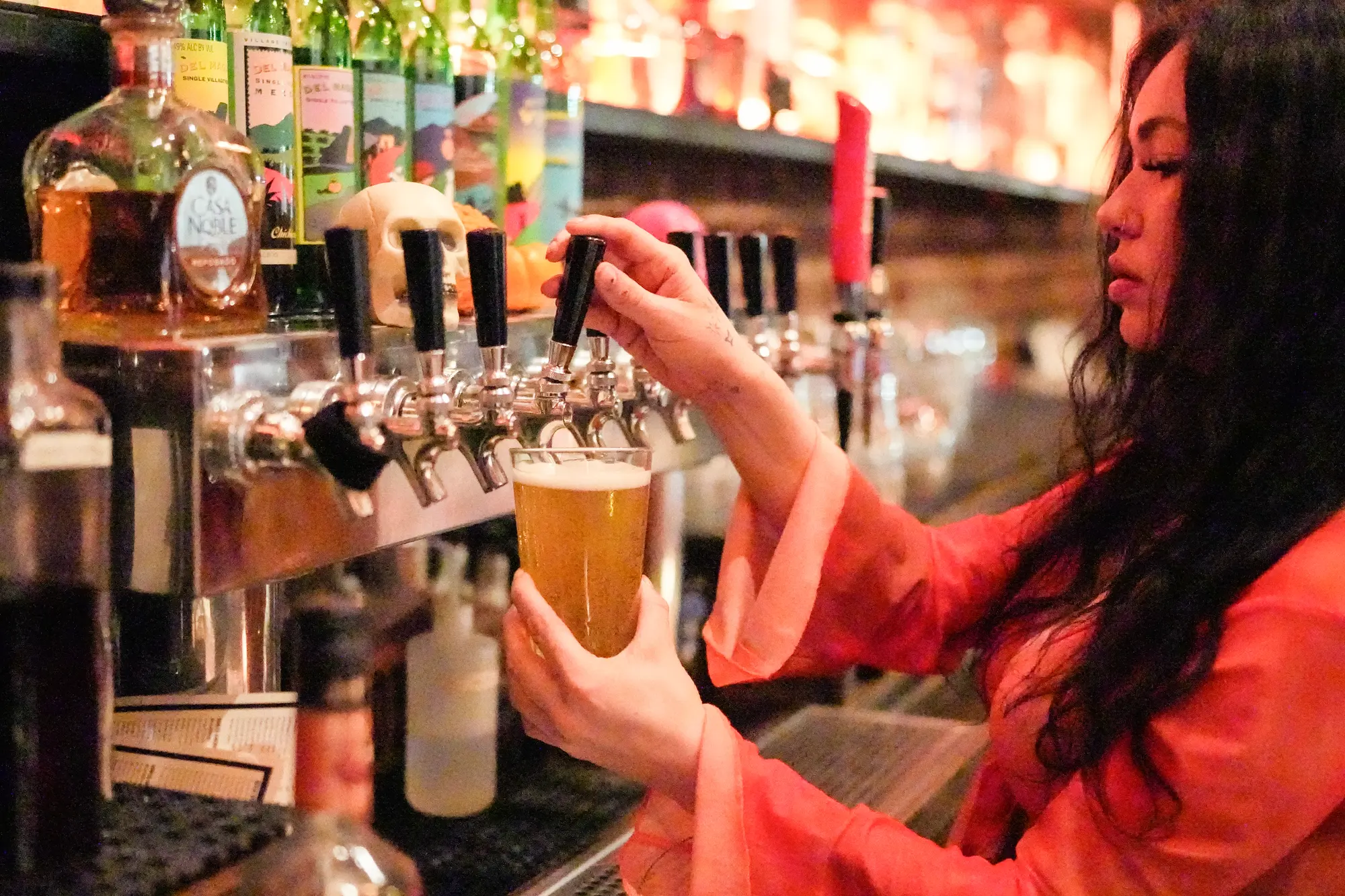 A bartender in an orange top pulls a pint of beer from a row of taps.