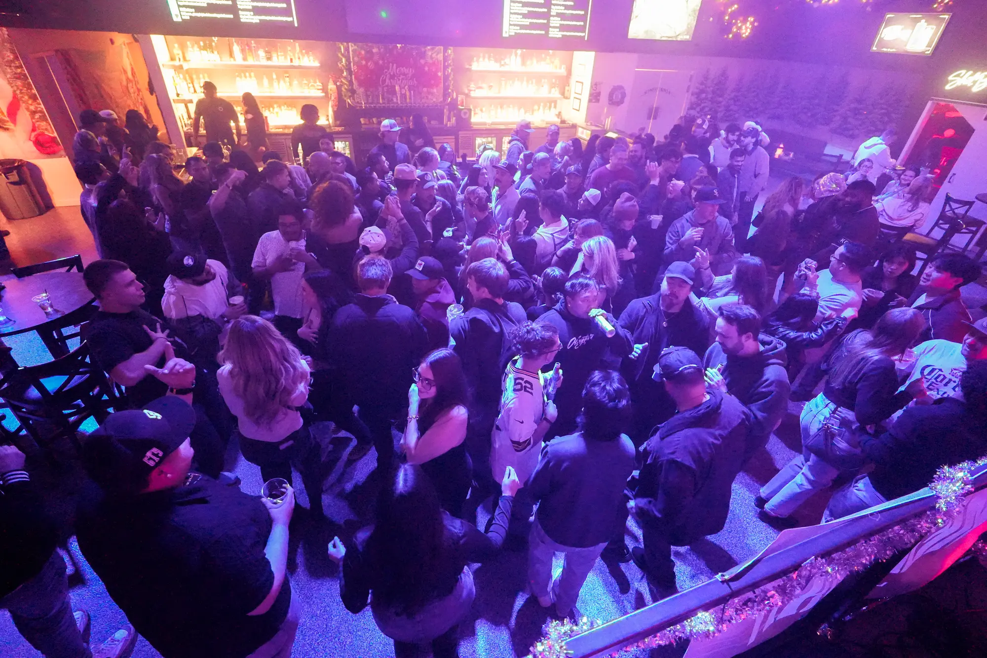 A packed dance floor seen from above at a holiday party, under purple and pink lights